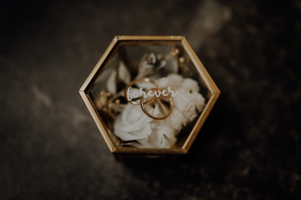 Detailaufnahme von Eheringen in einer goldenen Ringbox mit der Aufschrift "forever" beim Getting Ready