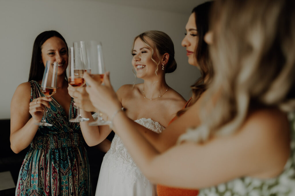 Braut stößt beim Getting Ready an ihrem Hochzeitstag mit ihren Freundinnen mit Sekt an