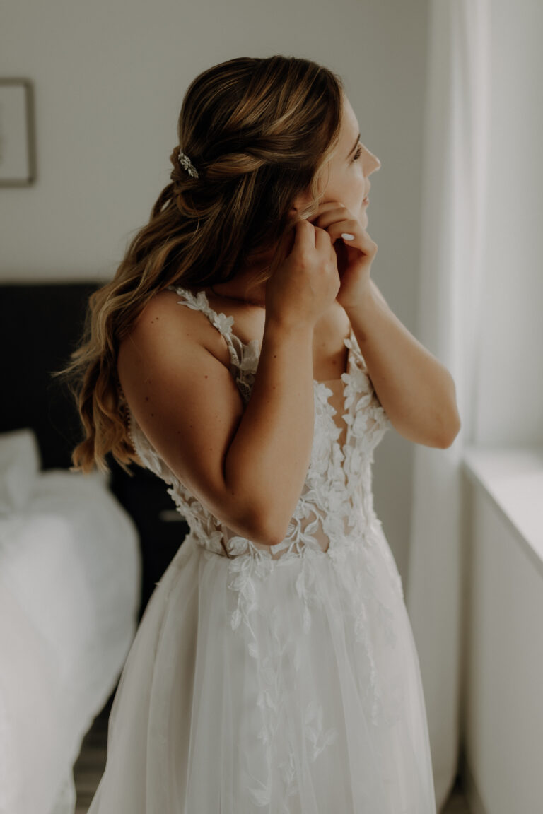 Braut zieht sich Ohrringe auf Hochzeitsfoto beim Getting Ready an