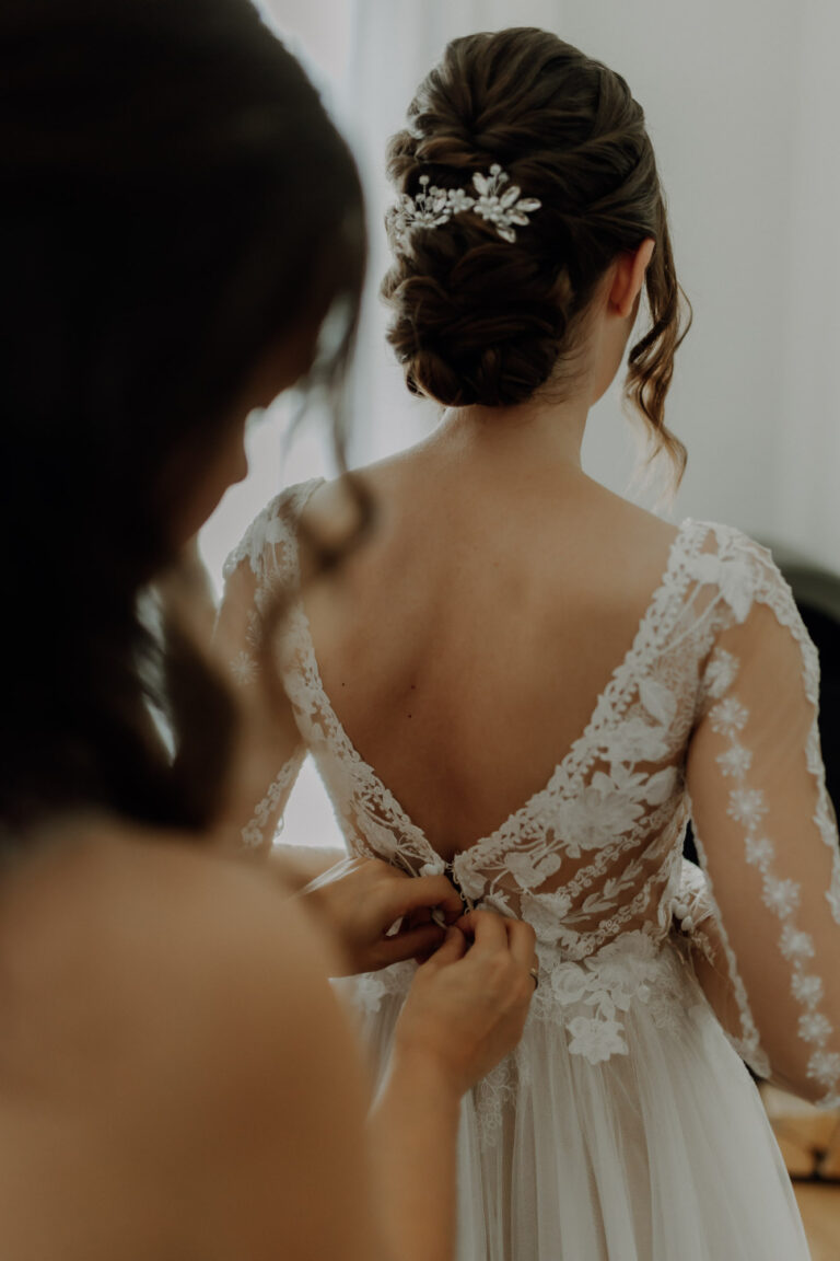 Trauzeugin knöpft Brautkleid beim Getting Ready am Hochzeitstag von der Braut zu