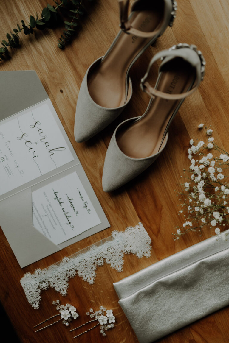 Detailaufnahme beim Getting Ready am Hochzeitstag von Brautschuhen, Einladungskarten und Strumpfband