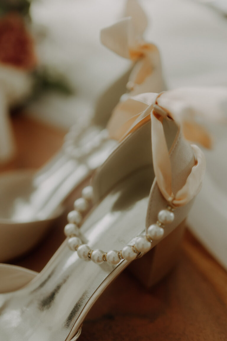 Detailaufnahme beim Getting Ready am Hochzeitstag von Brautschuhen mit Perlen und Schleife